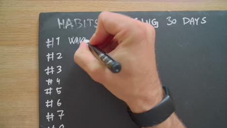 Man Writing Wake Up Early on Blackboard Of Habits Stacking 30 Days
