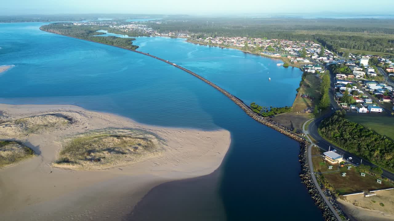 Drone aerial landscape of Harrington break wall crossing over Manning River ecosystem and sandy dune formations with local town housing main road and coastline near Taree Australia infrastructure