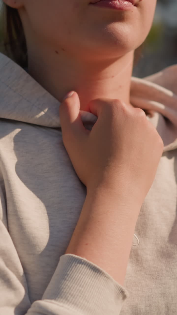 Close-up of woman s hand gently holding hoodie, with sunlight casting a warm glow on her face, the background is blurred, featuring an empty stadium and trees
