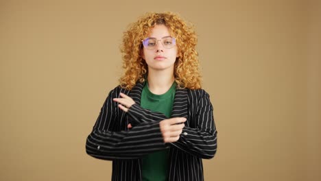 Portrait of a young woman with curly hair and glasses crossing her arms