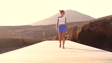 Cute-woman-walking-at-wooden-tables-against-mountain-range