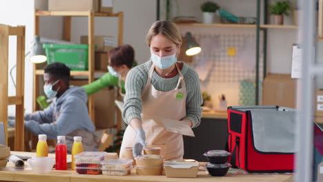 young woman in mask packing order at healthy food delivery service