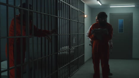 el oficial de la prisión encierra al criminal con el uniforme naranja en la celda de la cárcel.