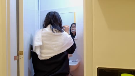 Asian-woman-with-wet-hair-brushing-her-teeth-in-front-of-mirror
