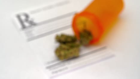 Slow-rack-focus-of-an-open-pill-bottle-spilling-marijuana-flowers-onto-a-blank-RX-sheet-on-a-white-table