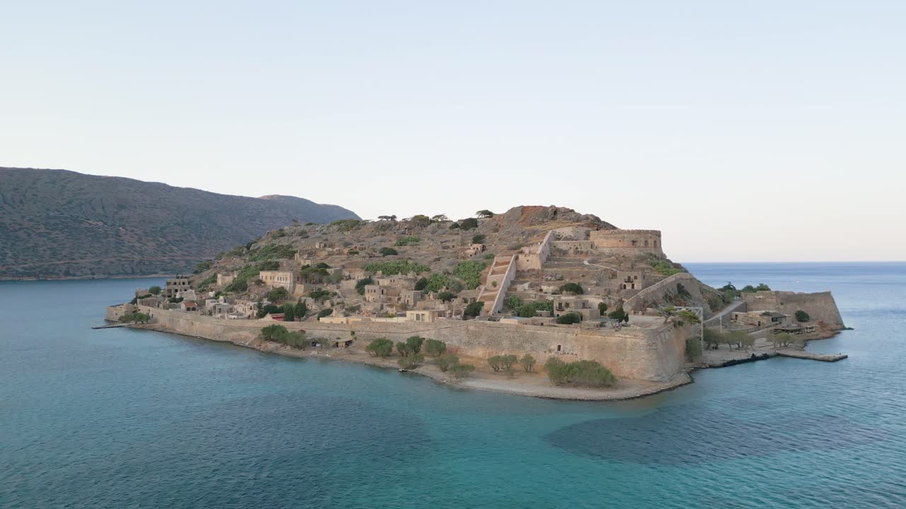 A cinematic orbit around the historic island of Spinalonga in soft afternoon light. Fortified walls, sea, and timeless beauty captured from above