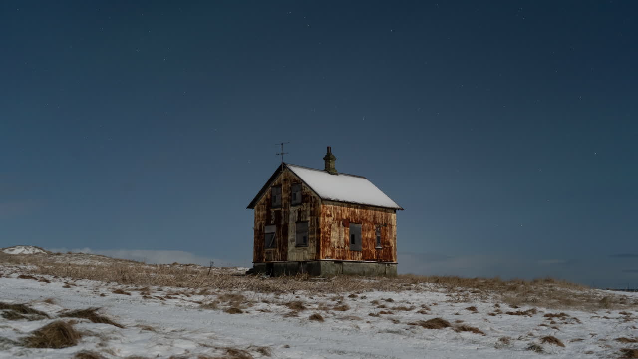 un timelapse de 12 segundos que muestra una amplia vista de una casa abandonada y oxidada en un paisaje invernal con la aurora danzante por encima.