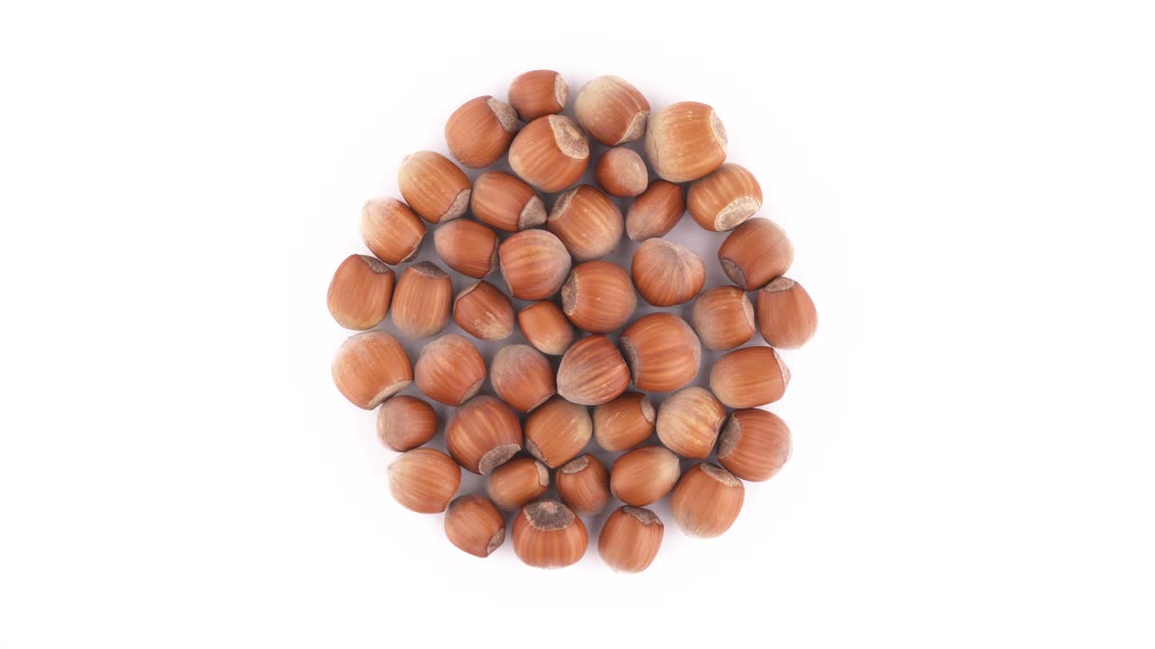 Top view from above of a circle shaped hazelnuts heap. Rotating on the turntable isolated on the white background. Close-up. Macro.