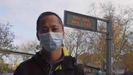 a sign reads 'stay home, save lives' behind a man wearing a mask during the coronavirus outbreak