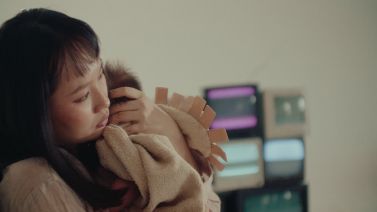 Mother Holding Newborn Baby Wrapped in Blankets While playing together standing in a living room with television on background