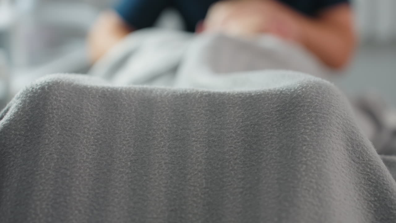 Patient covered in striped grey blanket lying on massage bed in bright spa room with soothing white background during relaxing wellness session highlighting cozy environment and tranquil atmosphere