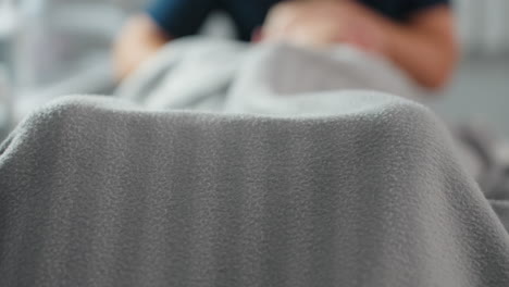 patient covered in striped grey blanket lying on massage bed in bright spa room with soothing white background during relaxing wellness session highlighting cozy environment and tranquil atmosphere
