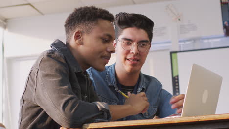 male teacher giving one to one support to student working at desk on laptop