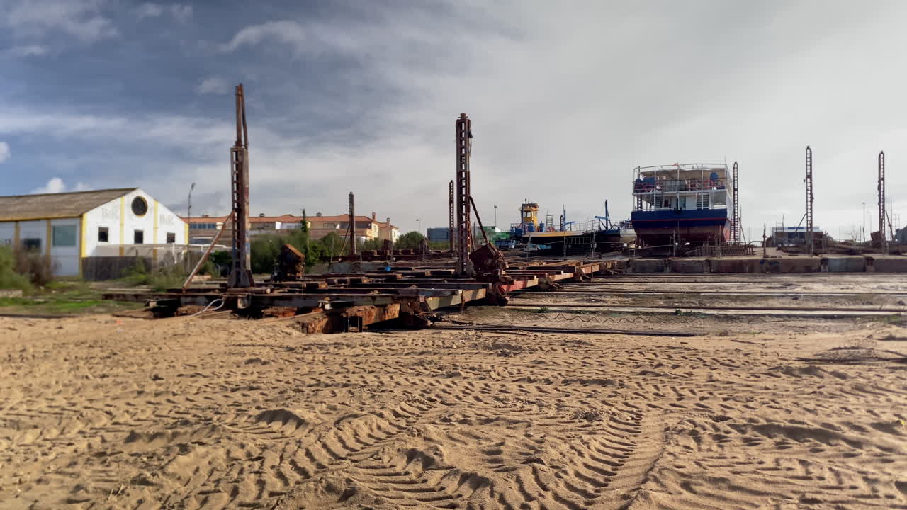 Cantiere navale di Sanlucar de Barrameda che presenta strutture di bacino di carenaggio, invasi per barche e una nave in costruzione sullo sfondo.