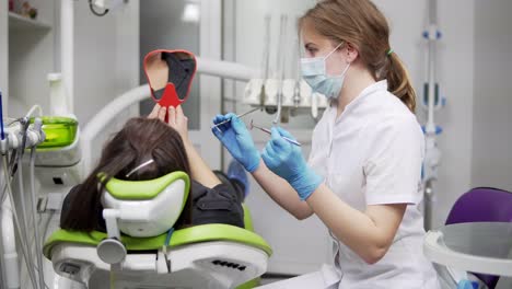 Estomatología.-Una-Joven-Dentista-Está-Hablando-Con-Un-Cliente-Y-Dándole-Un-Espejo.