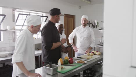 chef masculino diverso instruyendo a un grupo de chefs masculinos aprendices usando una tableta en la cocina, en cámara lenta