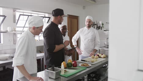 diverse male chef instructing group of trainee male chefs using tablet in kitchen, slow motion