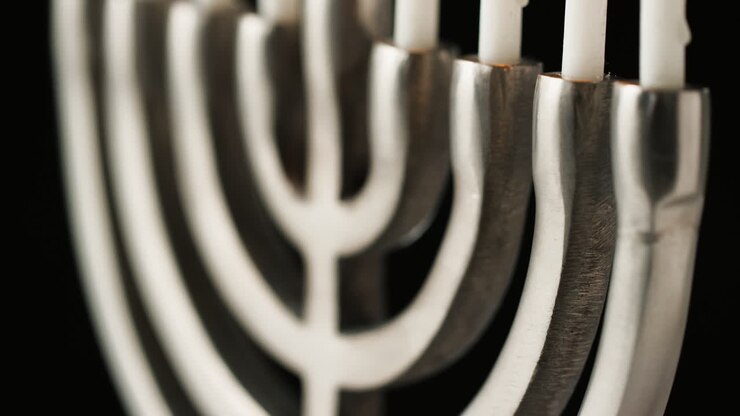 Close up, shallow depth of field tilt shot of silver menorah at an angle, with white lit candles