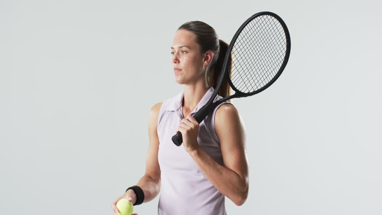 젊은 백인 여성이 테니스 라켓을 들고 자신감 있게 포즈를 취합니다.