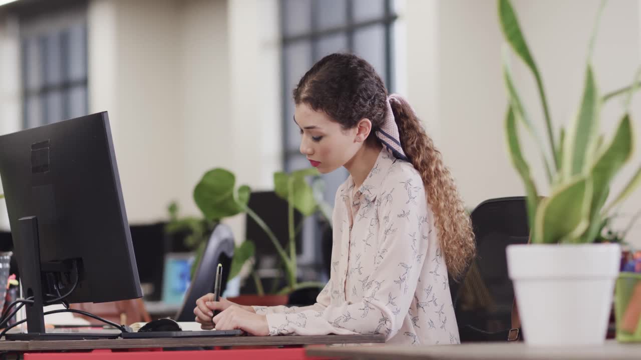 feliz mujer biracial creativa usando una tableta en una oficina casual, en cámara lenta