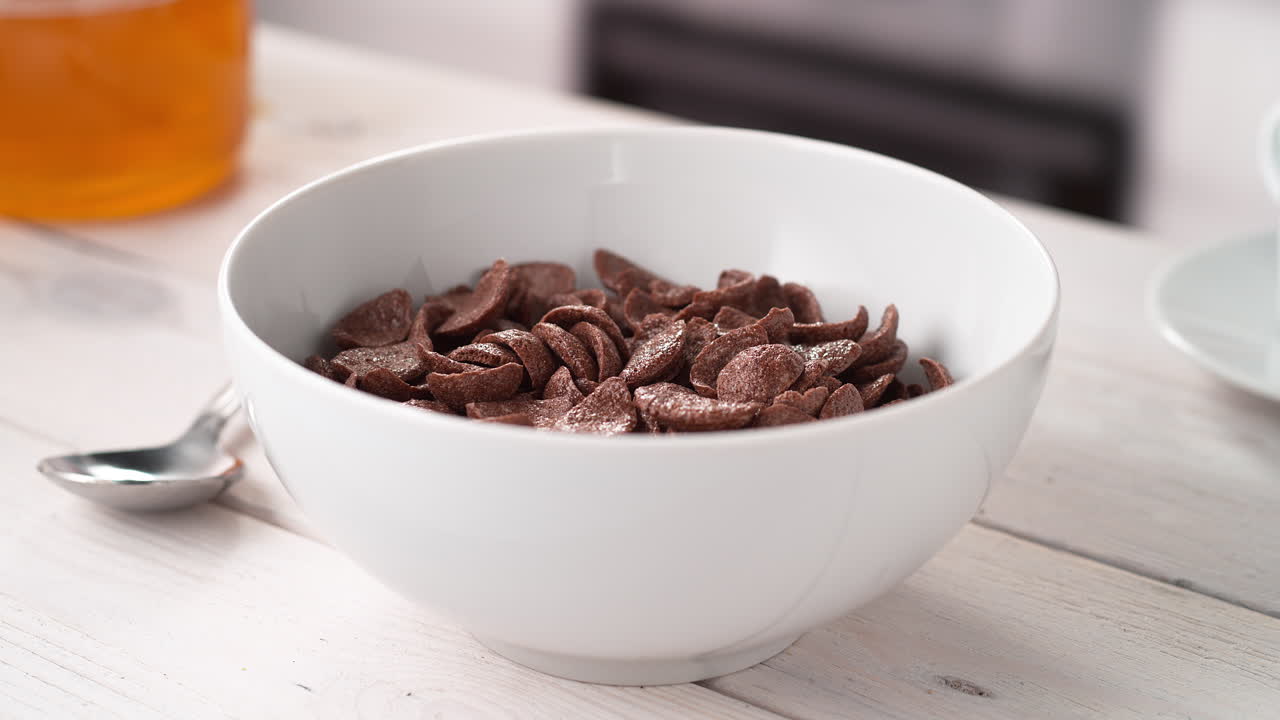 아침 식사를 준비: 부 테이블에 놓인 카카오 데기 모양의 시리얼이 있는 그에 우유를 부어, 느린 동작