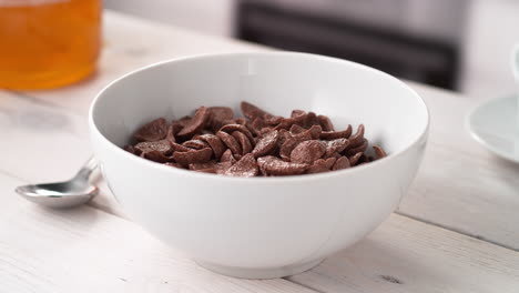 preparar el desayuno: verter leche en un cuenco de cereales en forma de concha de cacao colocados en una mesa de la cocina, en cámara lenta