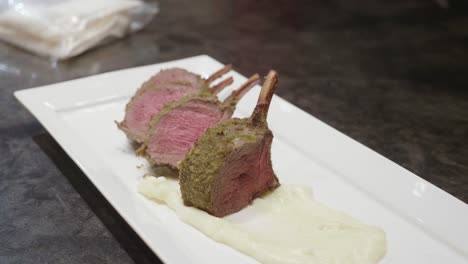 venison meat ribs slices, with green spice on top, plated on a white plate with mashed potato