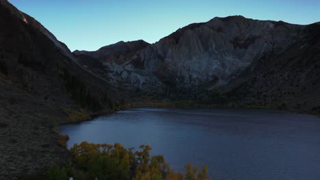 convict lake canyon trail mammoth lakes mountain aerial drone california autumn fall late afternoon shaded rugged valley peaks yellow aspen birch trees clear skies sierra nevada range upwards motion