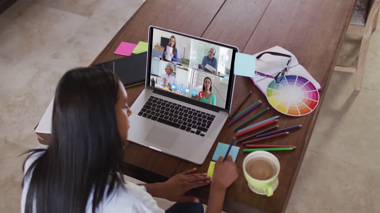 mujer caucásica usando una computadora portátil en videollamada con colegas y tomando notas