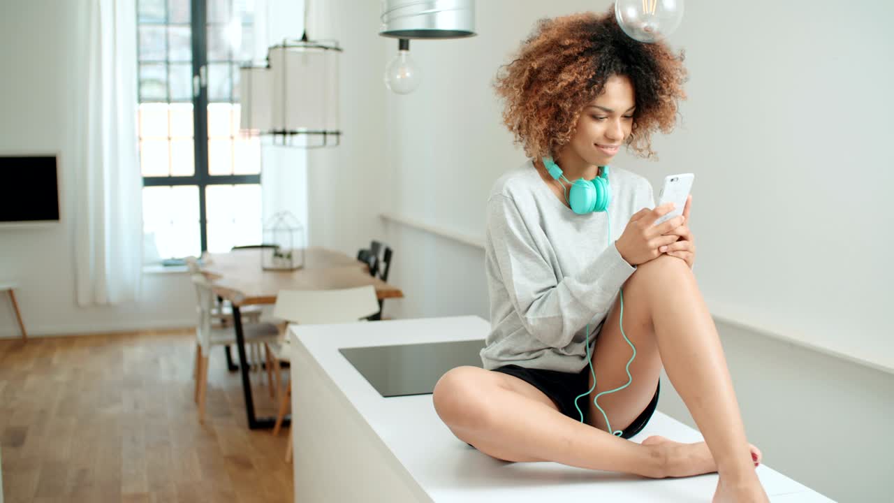 una hermosa joven afroamericana enviando mensajes de texto por teléfono móvil en casa.