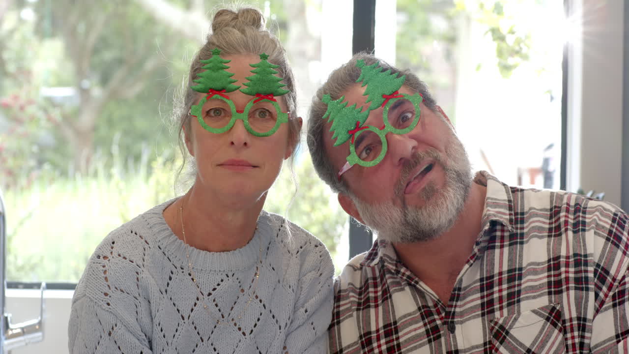 Mature couple making funny faces wearing festive Christmas glasses at home