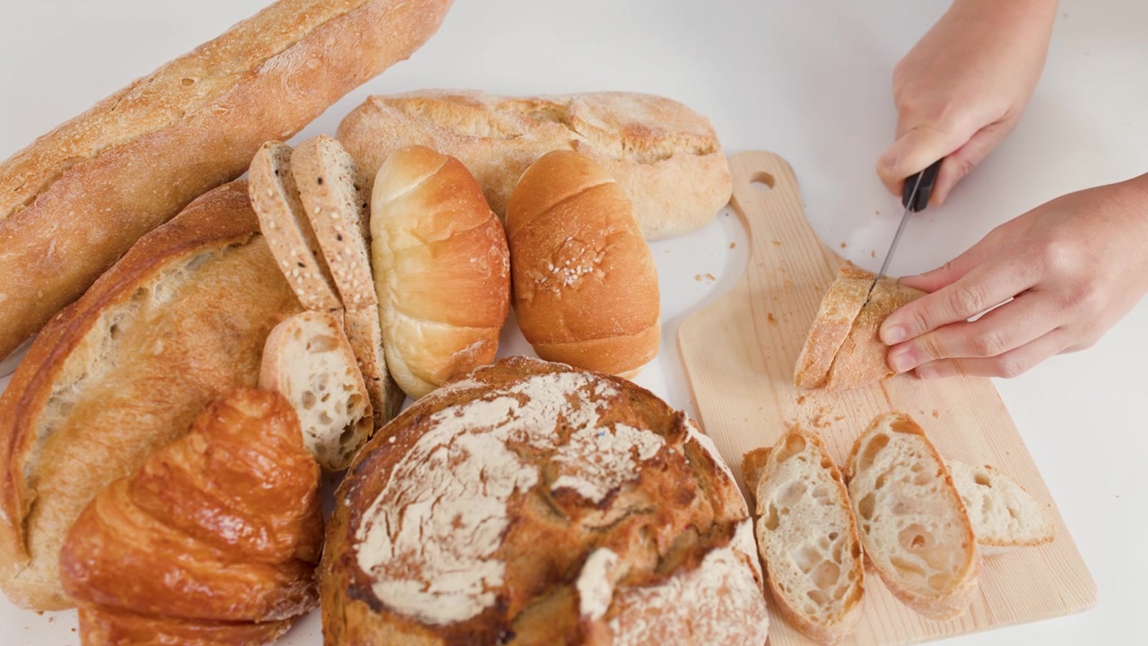 Person Slicing Fresh Bread on a Wooden Cutting Board