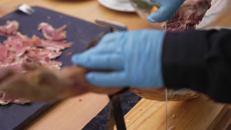 slicing traditional cured ham with knife and gloves at food preparation table