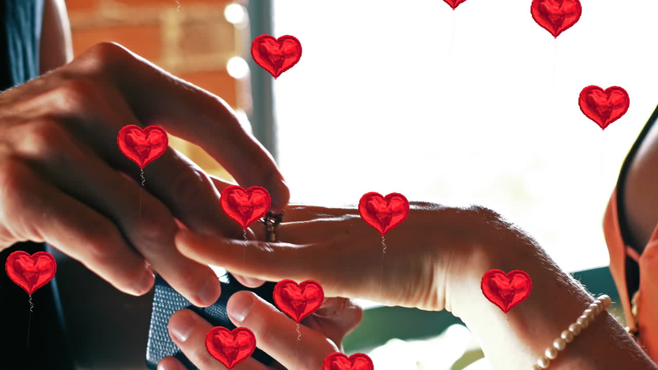 Multiple heart balloons floating against mid section of man putting ring on woman