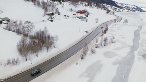 cars driving on the road passing by houses and fields covered with snow at winter in haugastol, norway