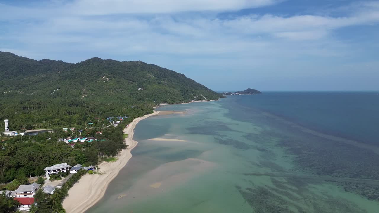 Scenic aerial view of Koh Phangan island showing coastline, sandy beach with crystal clear water, lush palm trees and seaside bungalows in tropical Thailand captured by drone on a sunny day
