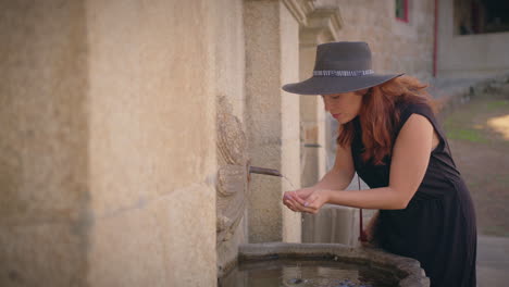 una chica se acerca a una fuente urbana y bebe agua en cámara lenta