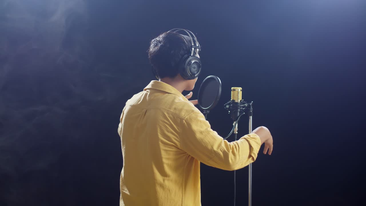 백색 연기 검은 배경에 콘덴서 마이크에 헤드폰을 하는 어린 소년의 뒷면