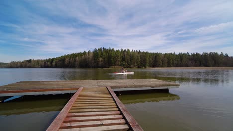 young man riding a pedal boat past a wooden pier on a pond surrounded by a wood