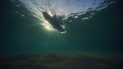 Silueta-De-Surfista-De-Tabla-Larga-Retroiluminada-Por-Los-Rayos-De-La-Mañana-Bajo-El-Agua