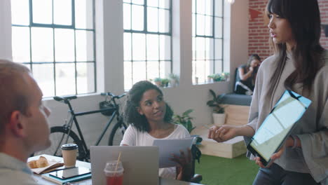 Jóvenes-Empresarios-Se-Reúnen-Con-Una-Mujer-Líder-Del-Equipo-Que-Presenta-Datos-Financieros-Usando-Una-Tableta-Que-Muestra-A-Diversos-Colegas-Ideas-De-Marketing-En-La-Presentación-De-La-Sala-De-Juntas-De-La-Oficina