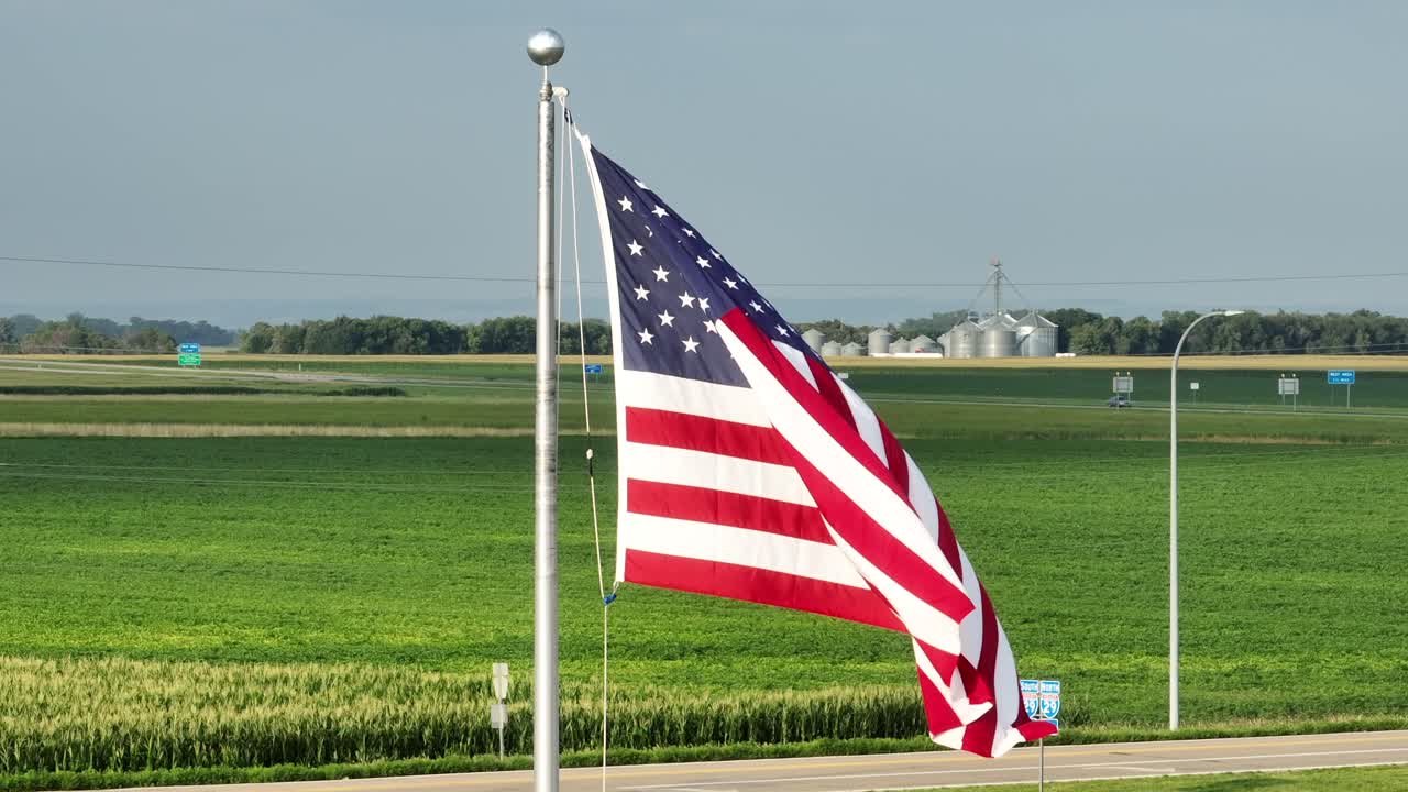 bandera estadounidense ondeando frente a campos de maíz y ascensores de grano en el medio oeste de los estados unidos