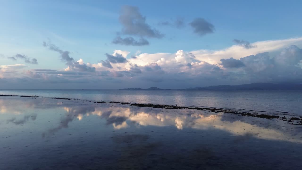 Drone footage of sunrise over Koh Phangan Thailand with clouds reflecting on the calm tropical sea and pink sunlight reflection