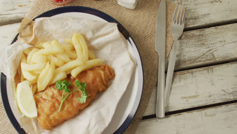 Video-of-fish-and-chips-on-plate,-salt-and-pepper-and-ketchup-on-wooden-table