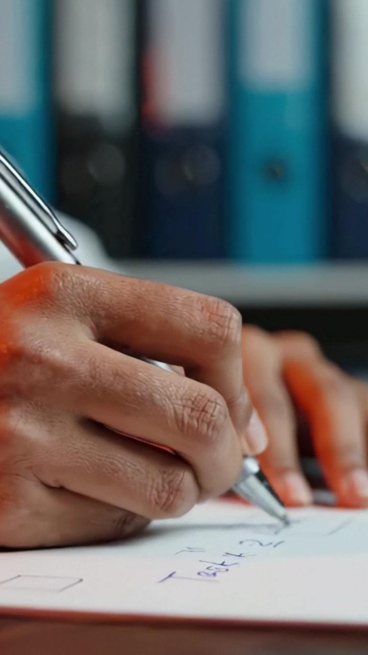 Scrittura a Mano Concentrata su Carta con una Penna, Primo Piano Dettagliato del Processo di Scrittura e dell'Ambiente d'Ufficio nell'Inquadratura, Sottolineando la Concentrazione e la Gestione delle Attività.