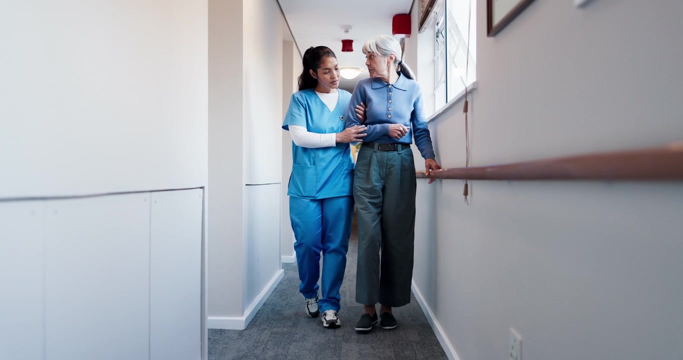 Nurse Assisting Elderly Woman Walking Down Hospital Hallway