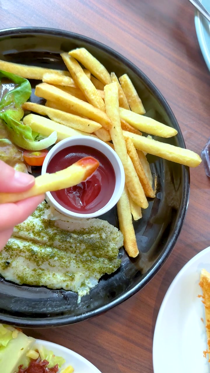 Una persona intinge patatine fritte dorate nel ketchup rosso a un tavolo di ristorante durante la cena.