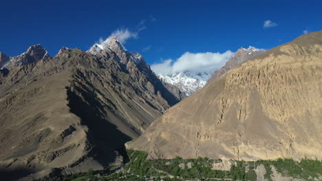 cinematic drone shot of tupopdan peak, passu cones in hunza pakistan, snow covered mountain peaks with steep cliffs and clouds forming on top, high rising wide aerial shot