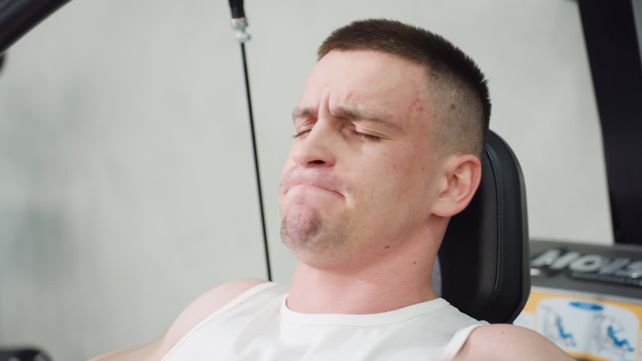 Close up sports man tightening face pulling handle of weight machine with strength moving up and down muscles straining effort intense workout focus veins visible sweat droplets on skin