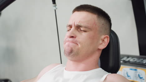 close up sports man tightening face pulling handle of weight machine with strength moving up and down muscles straining effort intense workout focus veins visible sweat droplets on skin
